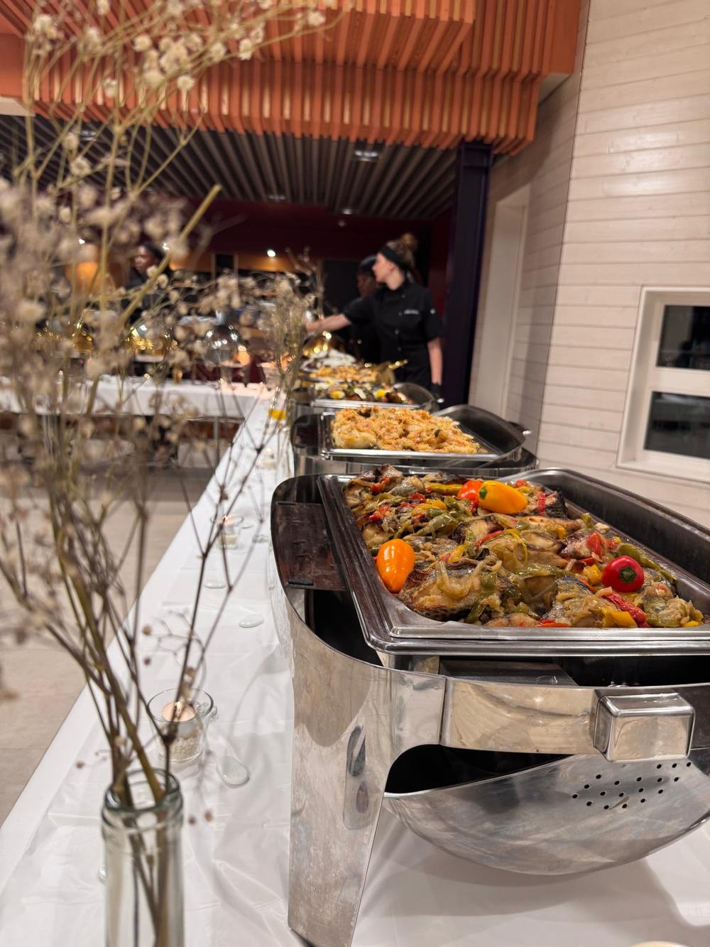 Buffet chaud Malewa dressé en bain-marie, avec des plats de poisson aux poivrons et un gratin, pendant que l'équipe en tenue noire sert