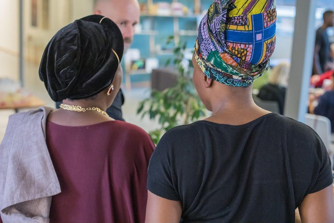 Deux femmes de dos, l'une en turban de velours noir, l'autre en foulard wax coloré