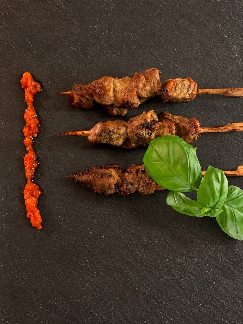 Trois brochettes de bœuf grillées, sauce pimentée et basilic sur une ardoise