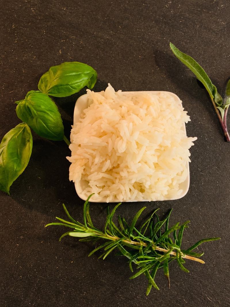 Riz parfumé dans un petit bol blanc, basilic et romarin sur une ardoise