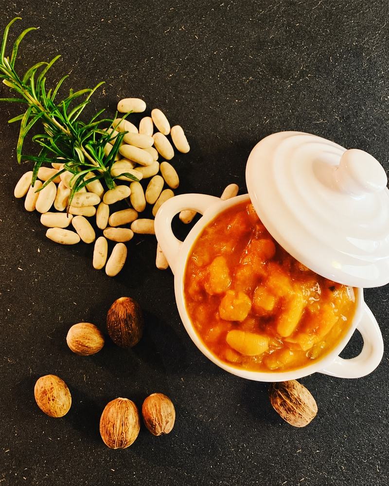 Haricots blancs en sauce dans une petite cocotte blanche, haricots secs et noix de muscade sur une ardoise