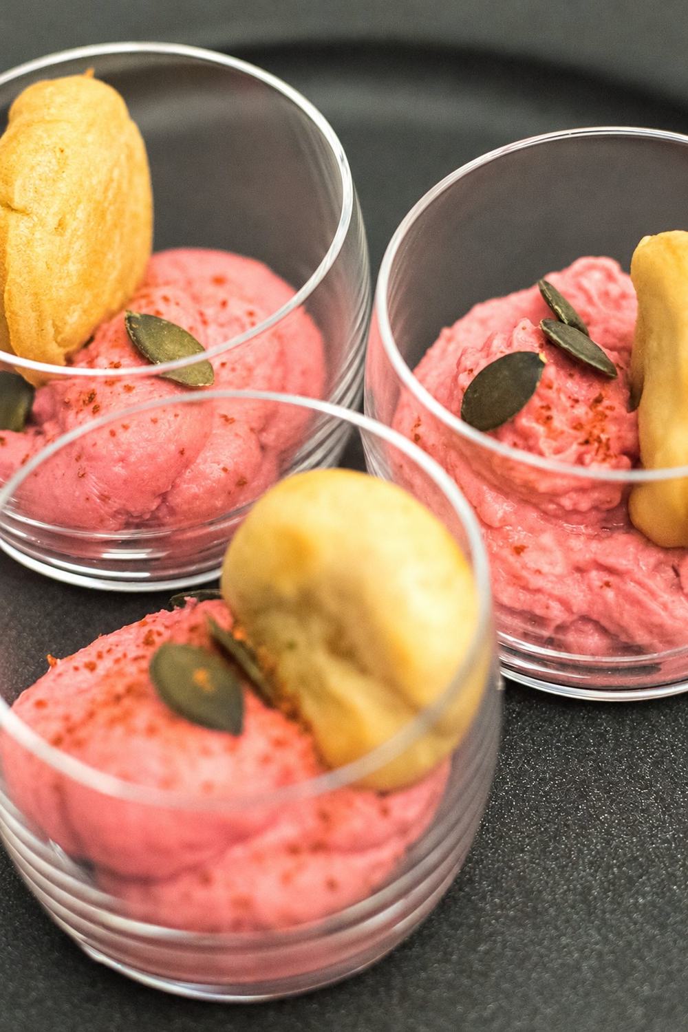 Trois verrines de mousse rose parsemée de graines de courge et de paprika, accompagnées d'un beignet doré